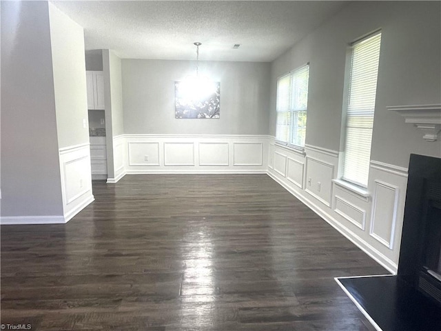 unfurnished dining area with a decorative wall, a textured ceiling, dark wood-style floors, and a wainscoted wall