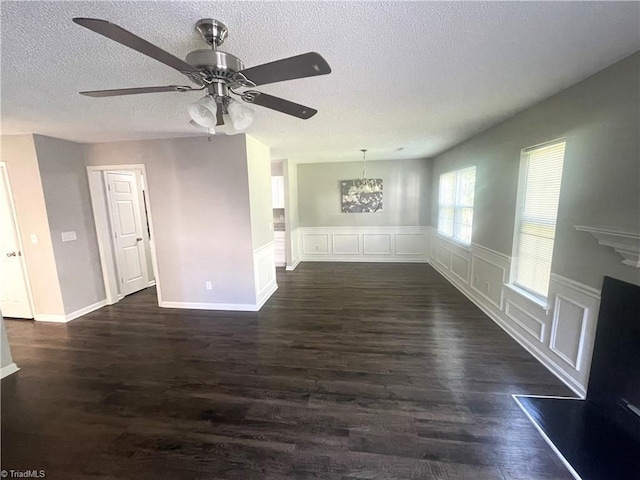 unfurnished living room featuring wainscoting, ceiling fan with notable chandelier, dark wood-style floors, and a textured ceiling