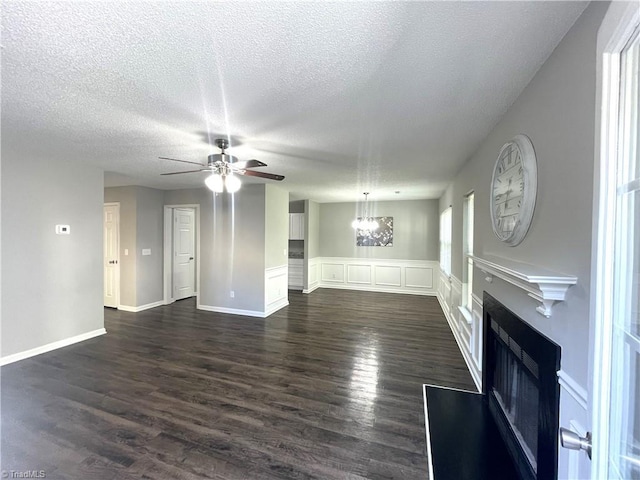 unfurnished living room with a fireplace with raised hearth, a textured ceiling, dark wood-style floors, and ceiling fan with notable chandelier