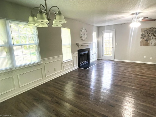 unfurnished living room with wainscoting, a fireplace, a textured ceiling, dark wood finished floors, and ceiling fan with notable chandelier