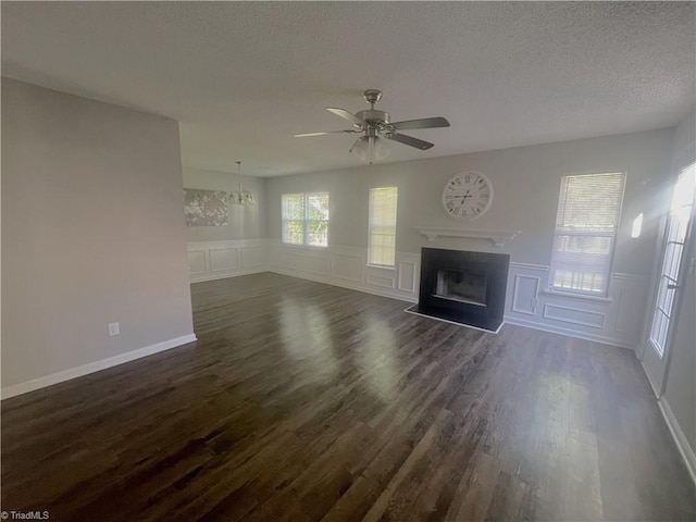 unfurnished living room featuring dark wood-style flooring, a decorative wall, a textured ceiling, a ceiling fan, and a fireplace with flush hearth