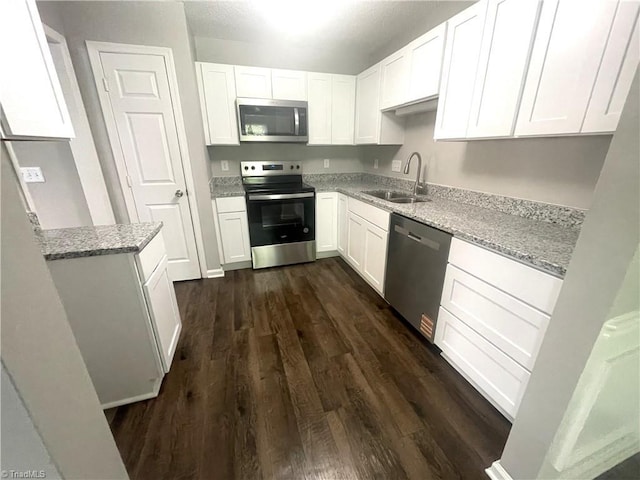 kitchen featuring light stone countertops, dark wood-type flooring, white cabinetry, a sink, and stainless steel appliances