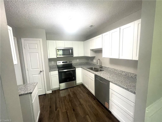 kitchen with a textured ceiling, appliances with stainless steel finishes, a sink, dark wood-style floors, and white cabinetry