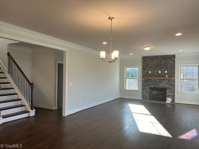 unfurnished living room with a notable chandelier, a stone fireplace, ornamental molding, and dark wood-type flooring