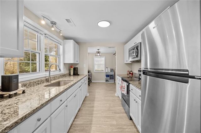 kitchen featuring light stone countertops, stainless steel appliances, sink, white cabinets, and light hardwood / wood-style floors