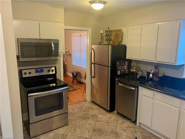 kitchen featuring dark stone countertops, appliances with stainless steel finishes, light wood-type flooring, and white cabinets