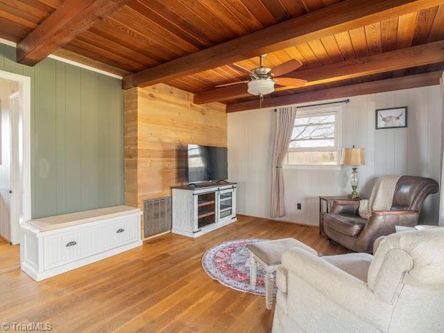 living room with a ceiling fan, wooden ceiling, beamed ceiling, and wood finished floors