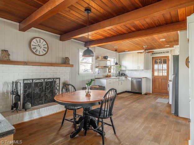 dining room featuring a brick fireplace, wooden ceiling, beamed ceiling, and light wood-style flooring