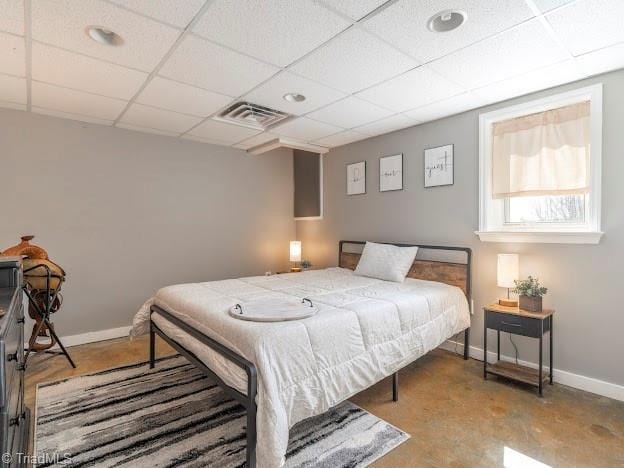 bedroom with concrete floors, a drop ceiling, visible vents, and baseboards