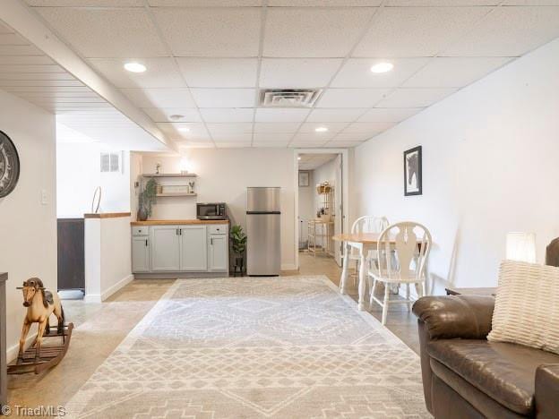 living area featuring baseboards, visible vents, a drop ceiling, and recessed lighting