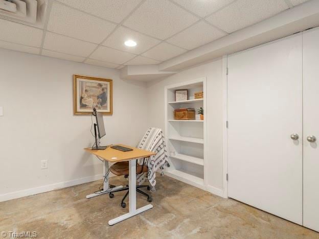 office area with built in shelves, a paneled ceiling, baseboards, and unfinished concrete floors