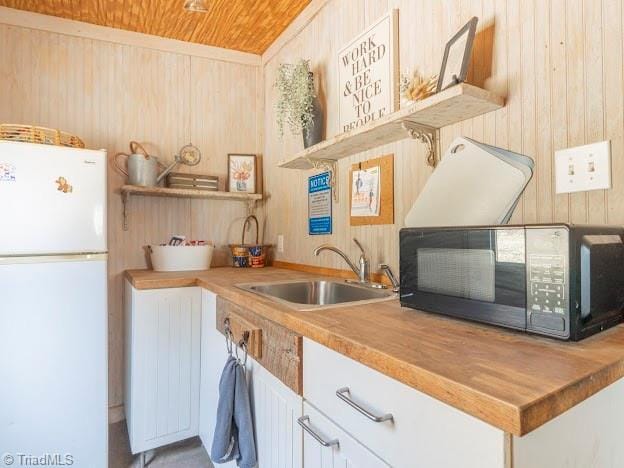 kitchen featuring black microwave, a sink, wooden counters, freestanding refrigerator, and open shelves