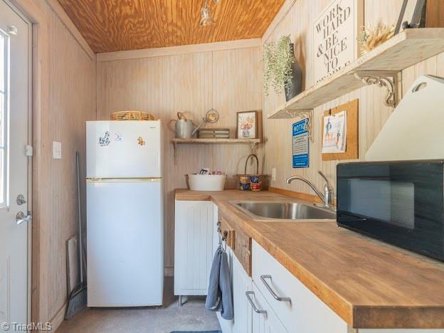 kitchen with black microwave, wooden ceiling, wooden walls, a sink, and freestanding refrigerator