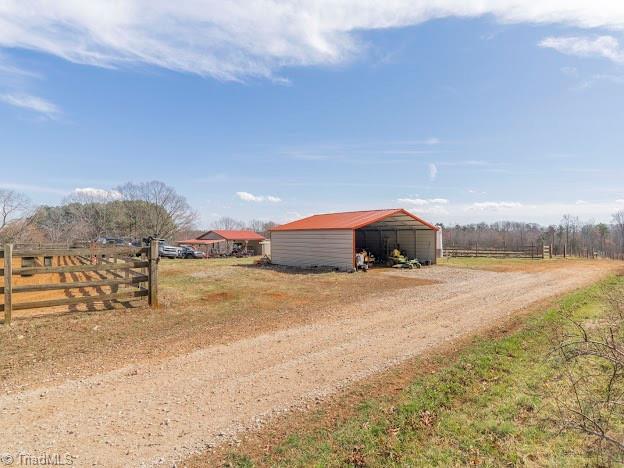 view of pole building featuring driveway, a rural view, and fence