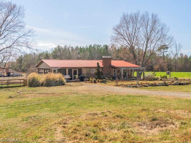 view of front of home with metal roof, a front lawn, a chimney, and fence