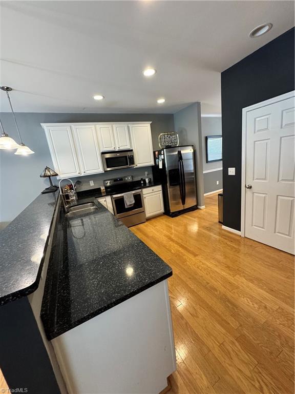 7213 Olmstead Dr, Burlington, NC 27215 - kitchen featuring stainless steel appliances, a sink, white cabinets, a peninsula, and light wood-style flooring