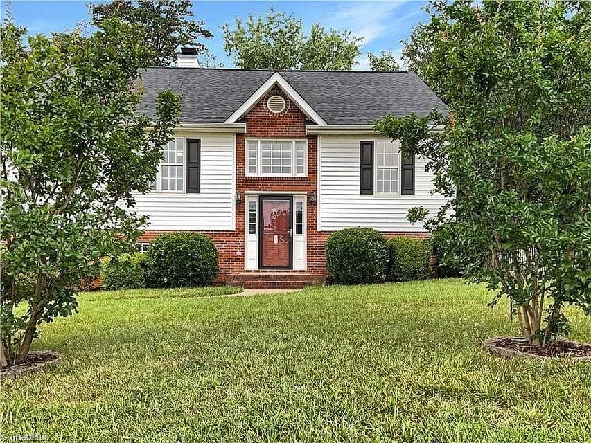 raised ranch featuring roof with shingles, brick siding, a front lawn, and a chimney