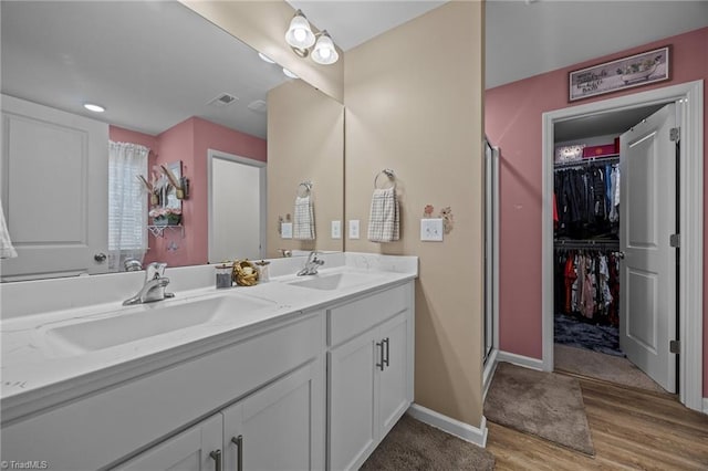 817 Sagemount St, Jamestown, NC 27282 - bathroom featuring wood finished floors, double vanity, a stall shower, a walk in closet, and baseboards