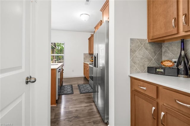 kitchen featuring dark wood-type flooring, tasteful backsplash, stainless steel appliances, brown cabinetry, and light countertops