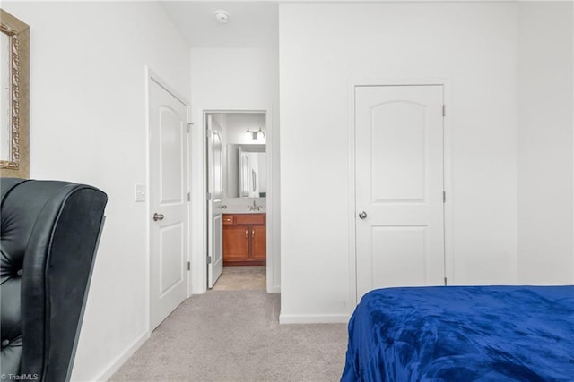 bedroom featuring light carpet, a sink, baseboards, and ensuite bathroom