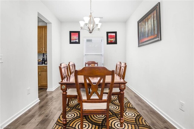 dining area with dark wood-style floors, a chandelier, and baseboards