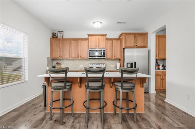 kitchen with appliances with stainless steel finishes, backsplash, light countertops, dark wood-style floors, and an island with sink