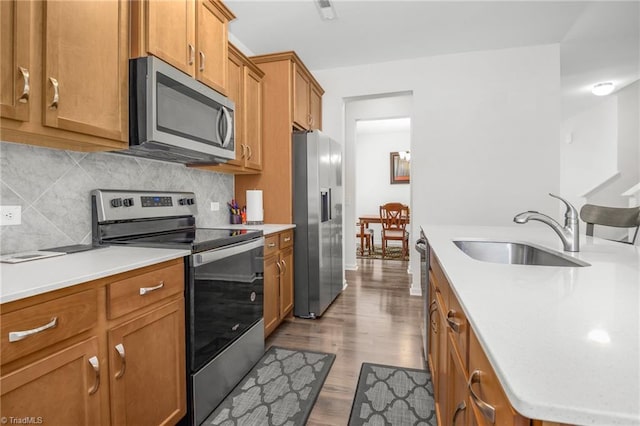 kitchen with stainless steel appliances, a sink, brown cabinetry, wood finished floors, and light countertops