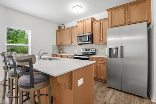 kitchen with appliances with stainless steel finishes, light countertops, backsplash, light wood-type flooring, and a kitchen breakfast bar