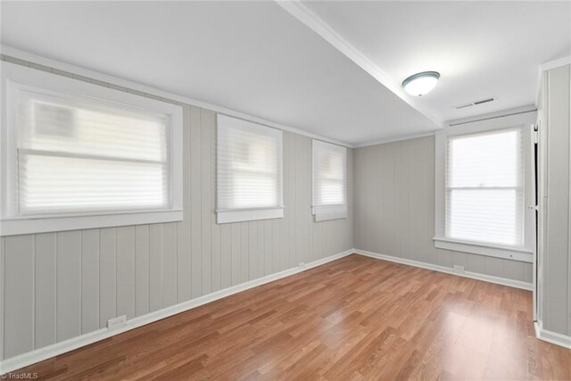 spare room with light wood-type flooring, wooden walls, and plenty of natural light