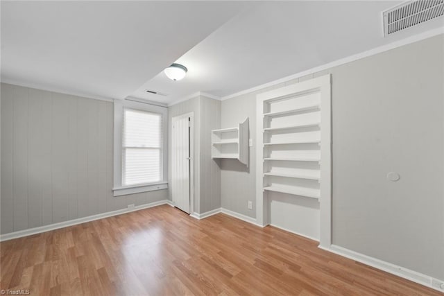 unfurnished room featuring wooden walls, light hardwood / wood-style floors, and crown molding