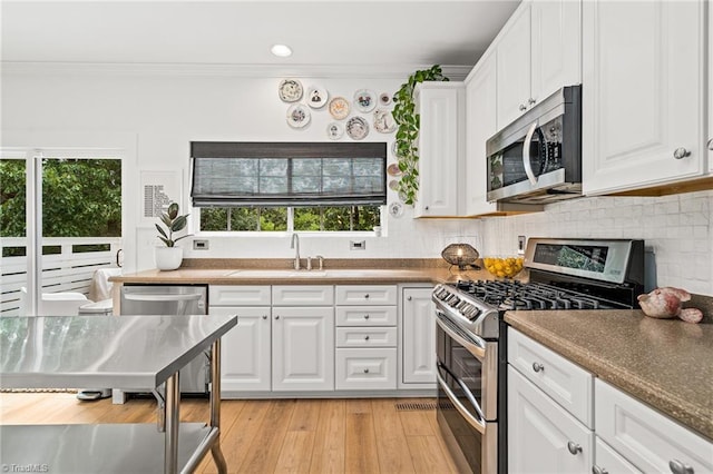 kitchen with white cabinets, stainless steel appliances, ornamental molding, and a sink