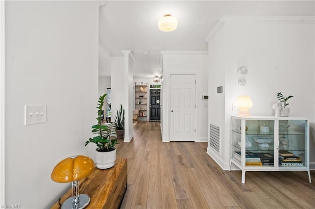 hall with baseboards, ornamental molding, wood finished floors, and visible vents