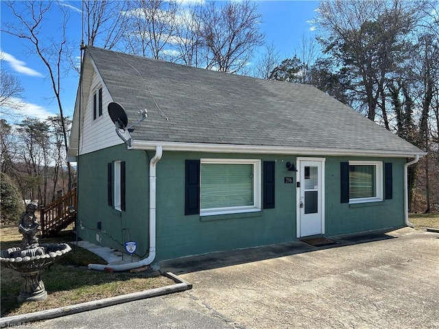 view of front of house featuring driveway, a shingled roof, and concrete block siding