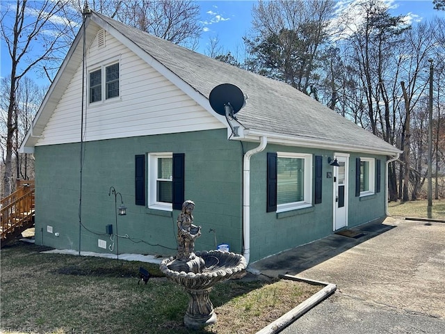 view of home's exterior with roof with shingles and concrete block siding