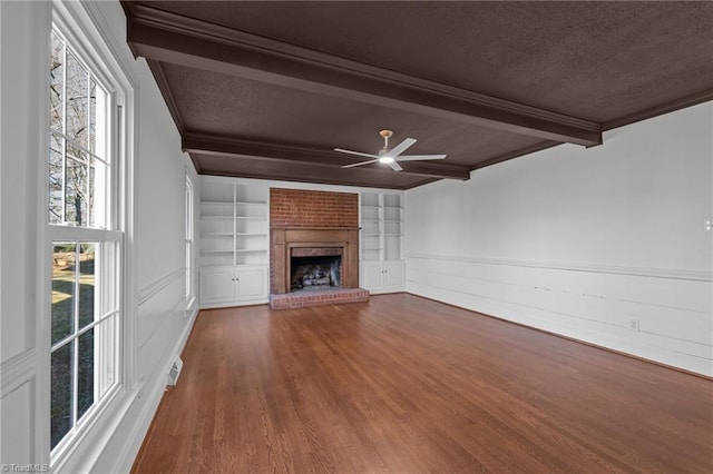 unfurnished living room featuring a wainscoted wall, beam ceiling, a ceiling fan, built in features, and wood finished floors