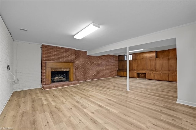 finished basement featuring light wood-style flooring, a fireplace, visible vents, and brick wall