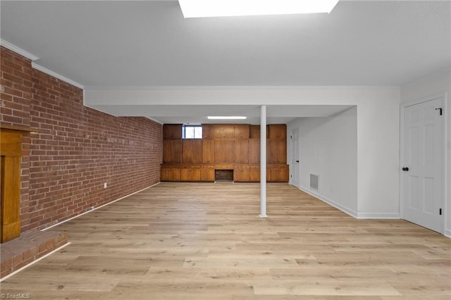 below grade area featuring visible vents, brick wall, crown molding, baseboards, and light wood-style flooring