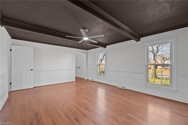 empty room with visible vents, beam ceiling, a textured ceiling, and wood finished floors