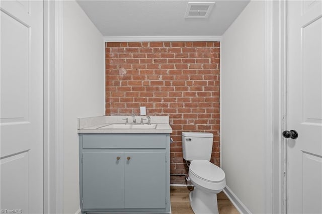 bathroom with visible vents, brick wall, toilet, wood finished floors, and vanity