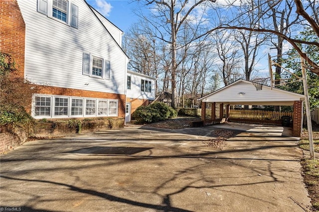 view of side of property with a detached carport, concrete driveway, fence, and brick siding