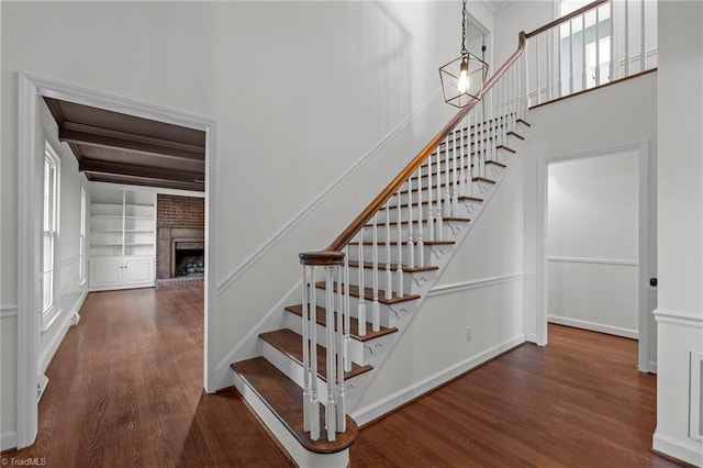 stairway featuring built in shelves, wood finished floors, visible vents, beam ceiling, and a brick fireplace