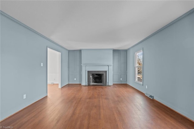 unfurnished living room featuring visible vents, a fireplace with flush hearth, wood finished floors, crown molding, and baseboards