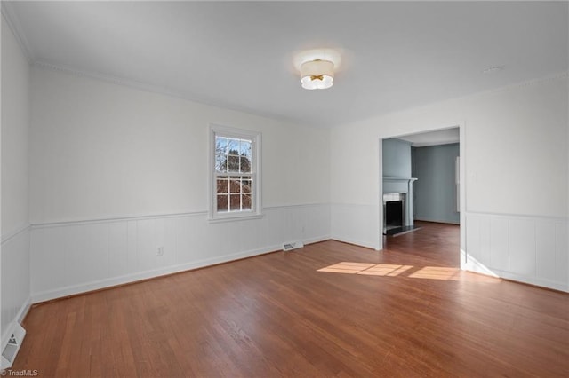 empty room with a wainscoted wall, a fireplace, visible vents, and wood finished floors