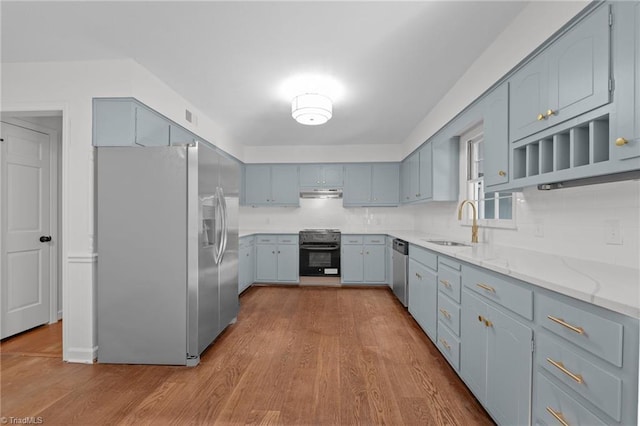 kitchen featuring a sink, light stone counters, under cabinet range hood, wood finished floors, and stainless steel appliances