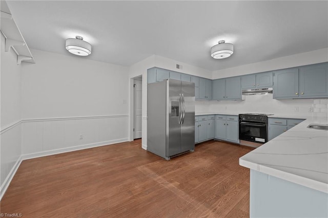 kitchen with dark wood-type flooring, under cabinet range hood, wall oven, stainless steel fridge, and light countertops