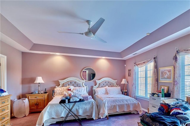 carpeted bedroom featuring ceiling fan and a raised ceiling