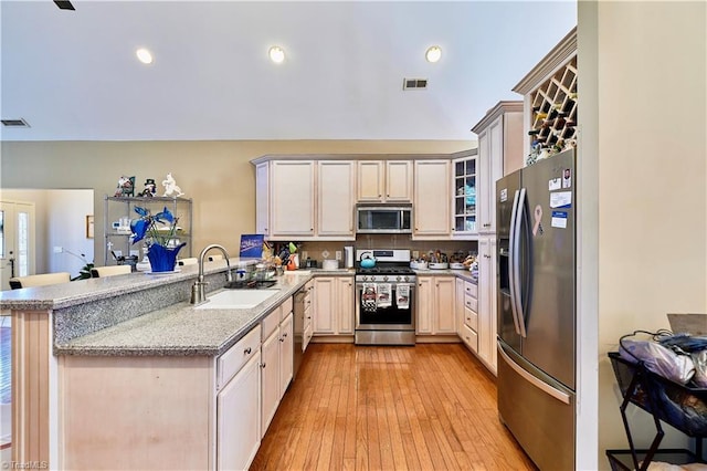 kitchen featuring stainless steel appliances, light stone countertops, kitchen peninsula, sink, and backsplash