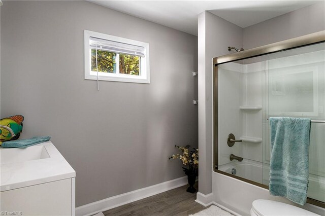 full bathroom with vanity, combined bath / shower with glass door, hardwood / wood-style flooring, and toilet