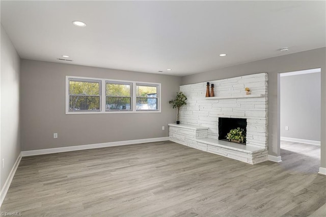 unfurnished living room featuring a stone fireplace and light wood-type flooring