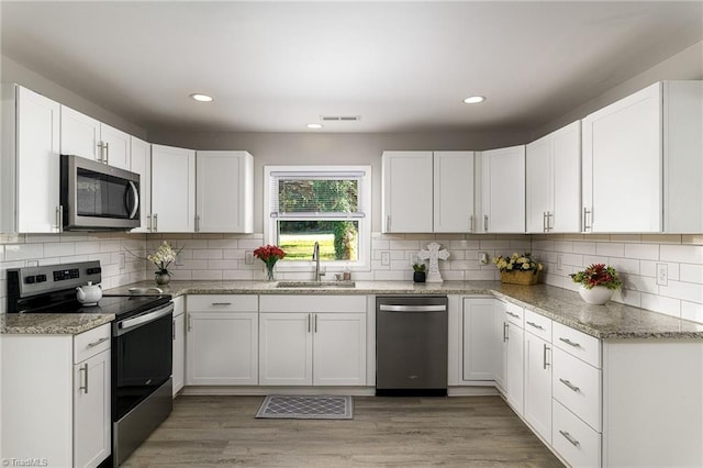 kitchen with appliances with stainless steel finishes, white cabinetry, hardwood / wood-style flooring, and sink